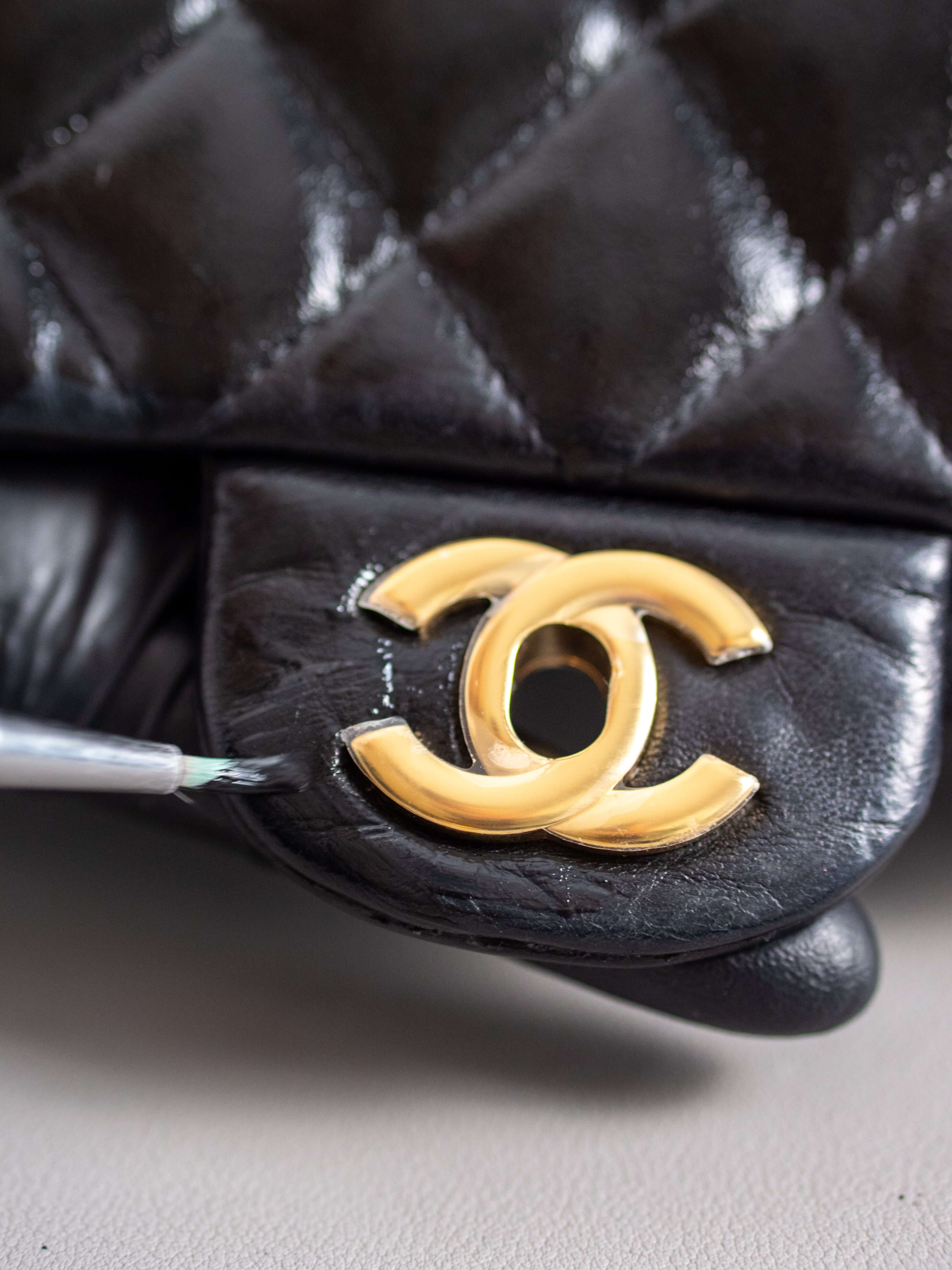 Artisan hand painting the logo area of a chanel classic flap handbag displaying the restoration process
