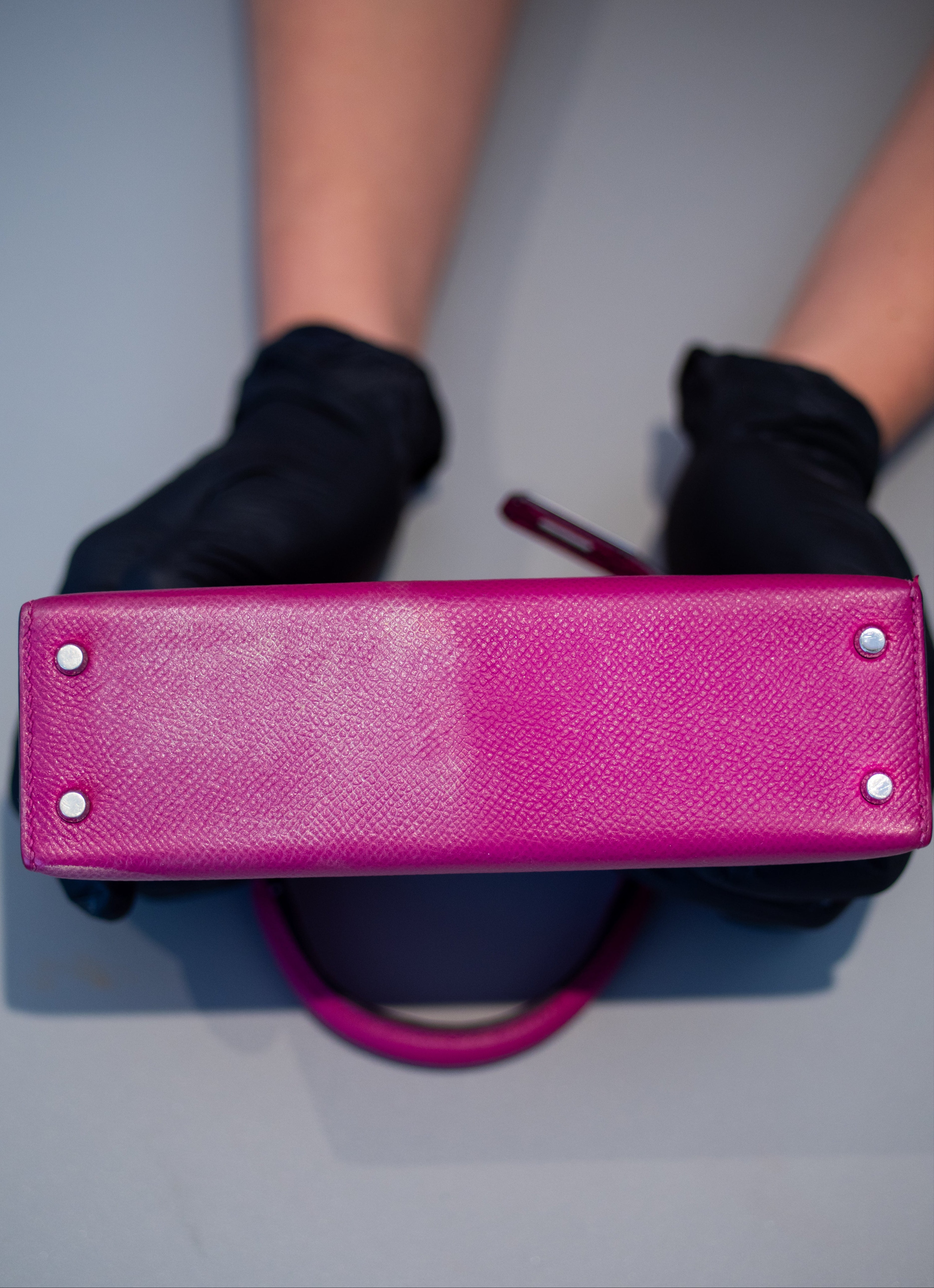 Person wearing black gloves holding a pink handbag on a gray background