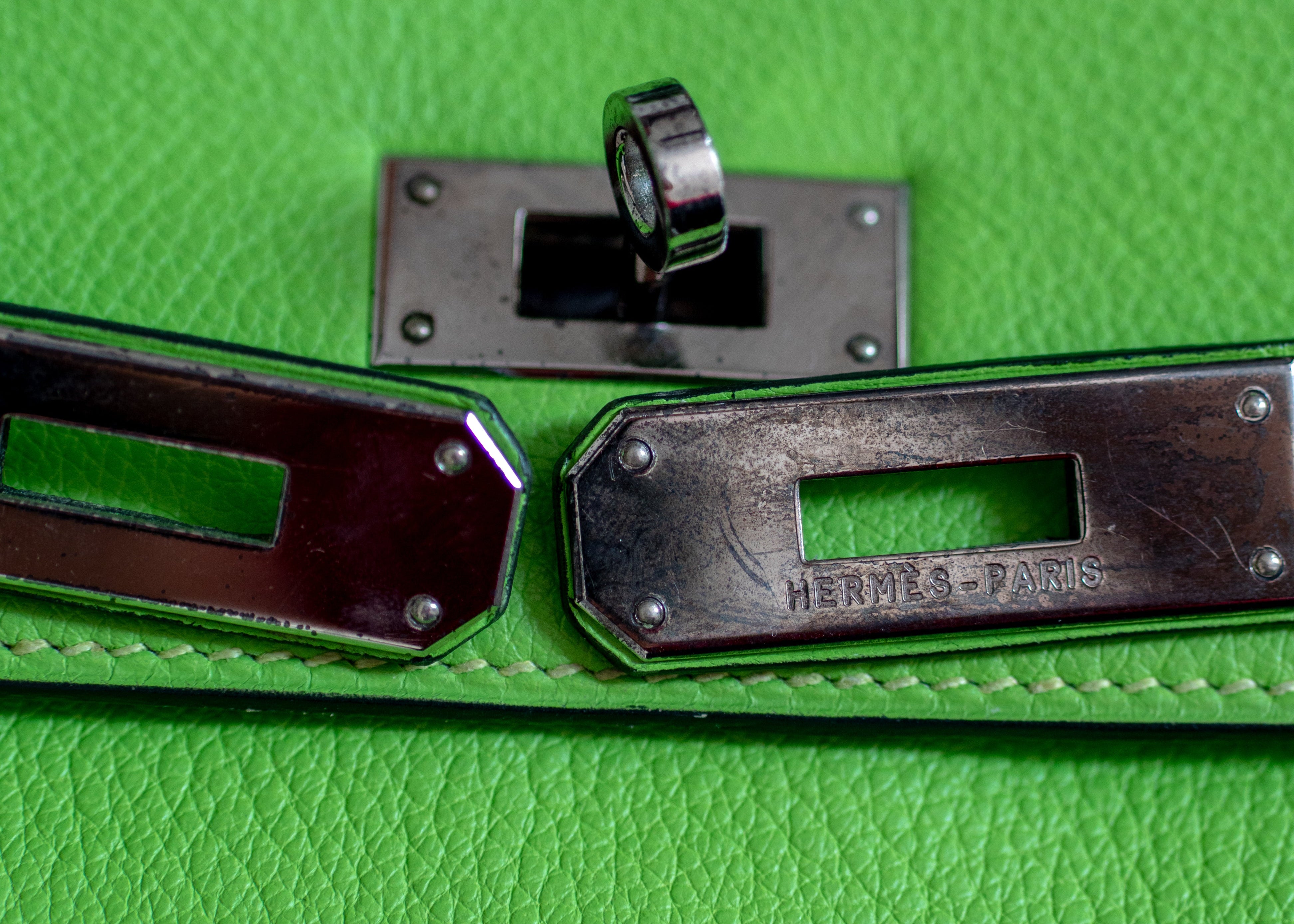 Close-up of a green leather handbag with metal hardware, featuring the brand name.