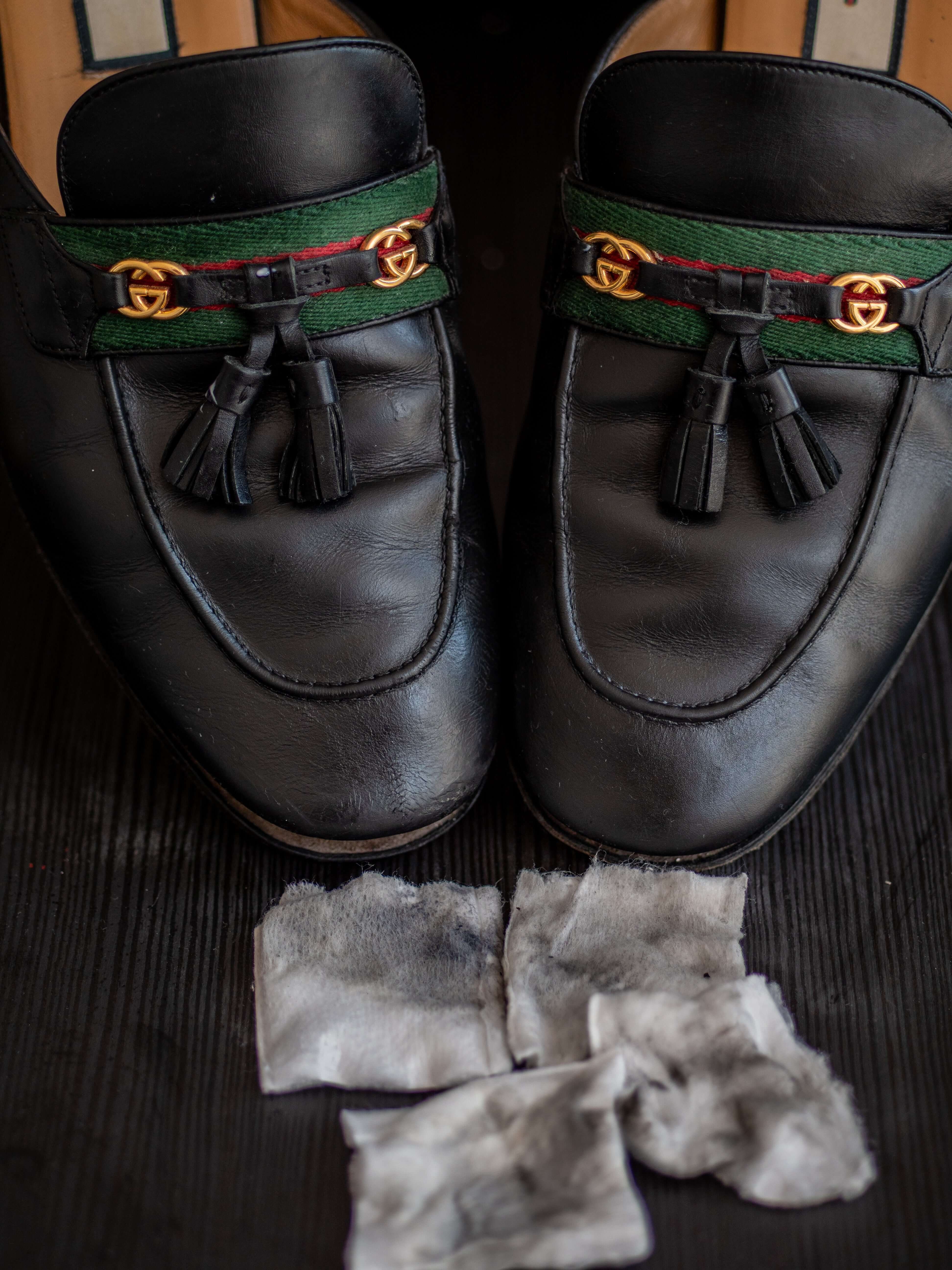Restored Gucci leather loafers after cleaning with leather balm, featuring polished finish, gold-tone logo hardware, and used cleaning pads with visible dirt