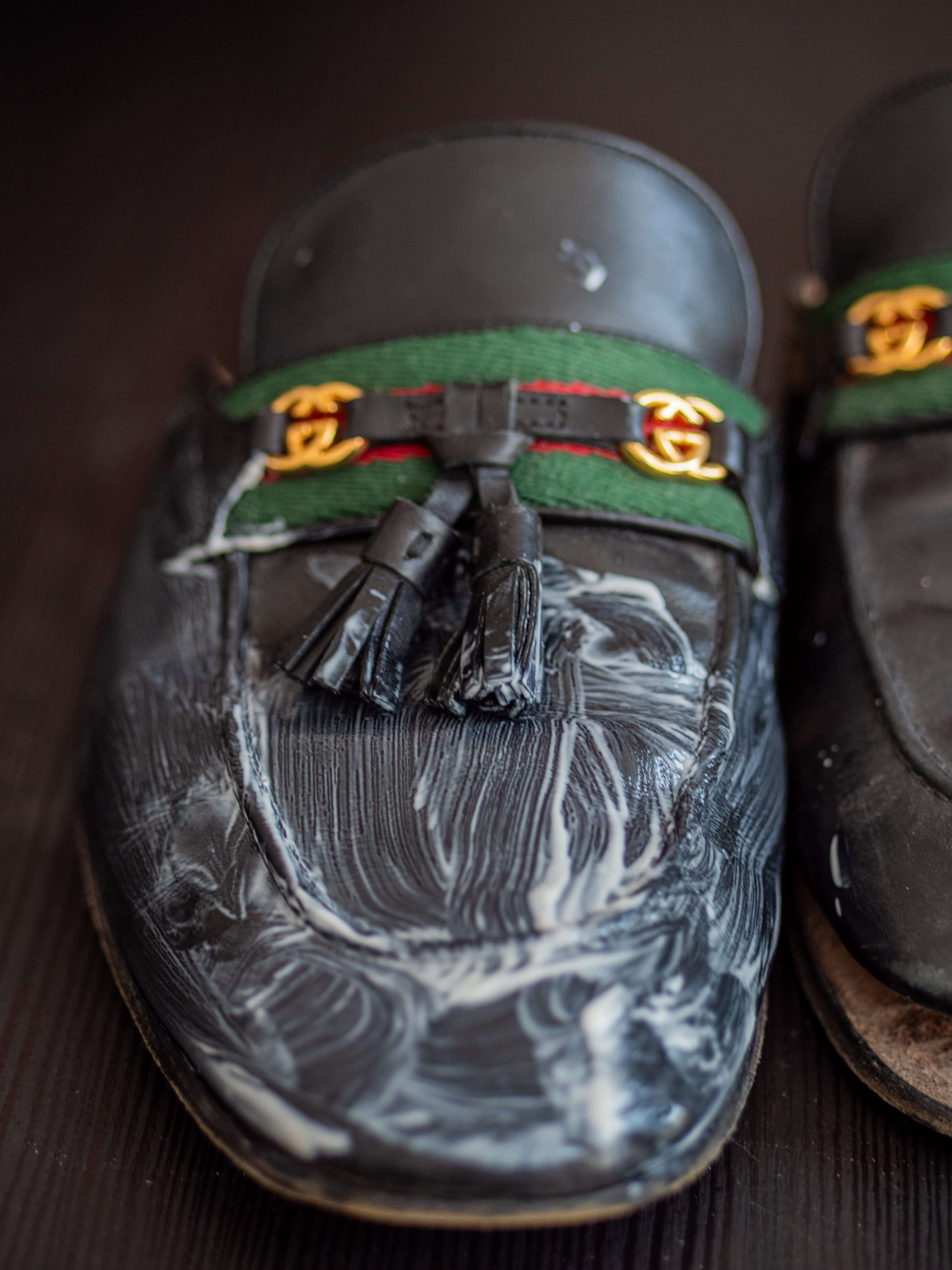 Gucci leather loafers being cleaned with leather balm, showing restoration process with cleaning agent applied to the shoe surface and tassel detail visible
