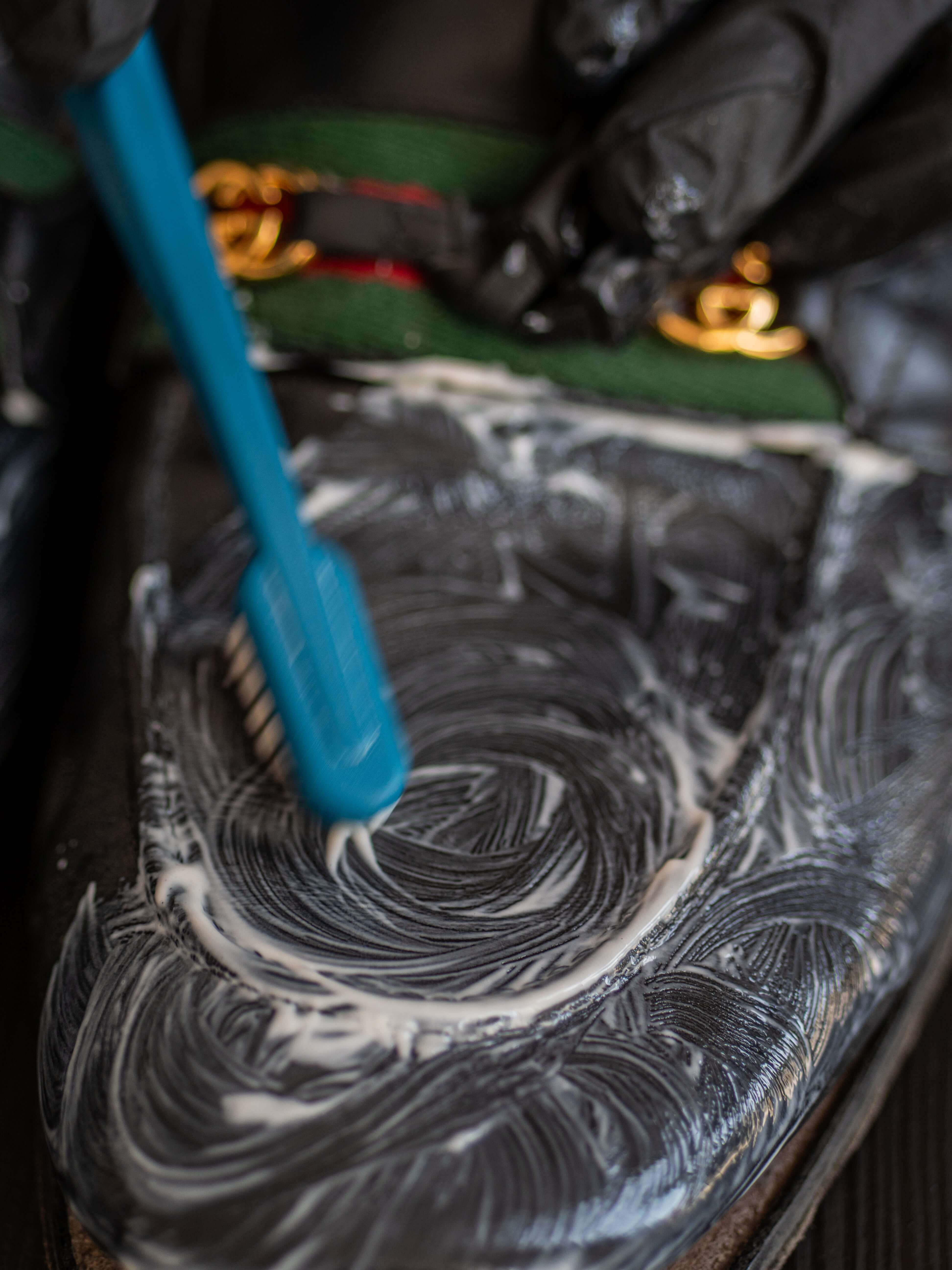 Gucci leather loafers being cleaned with leather balm, showing restoration process with cleaning agent applied to the shoe surface and tassel detail visible
