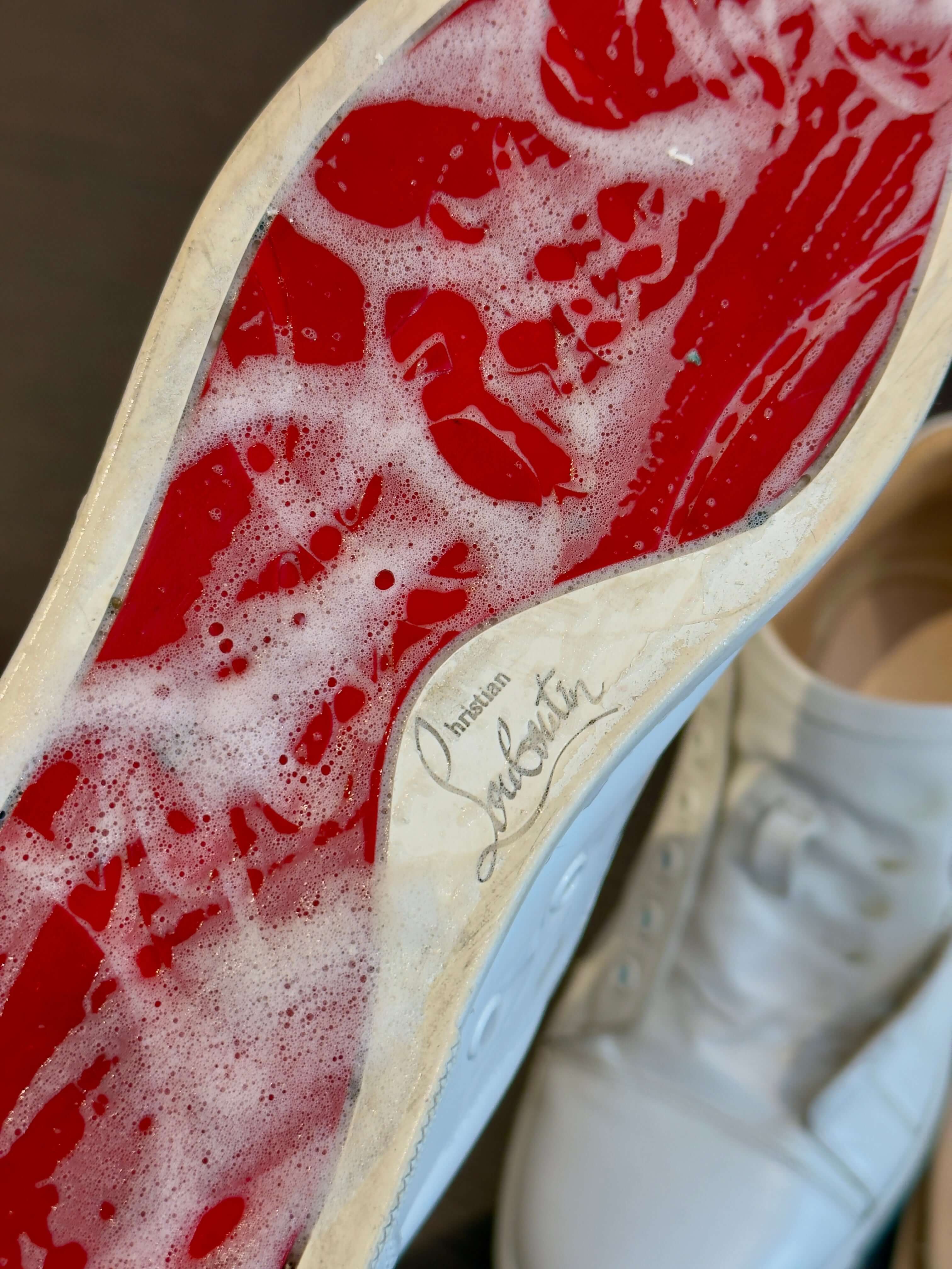 red sole of a louboutin sneaker being cleaned with a soapy solvent