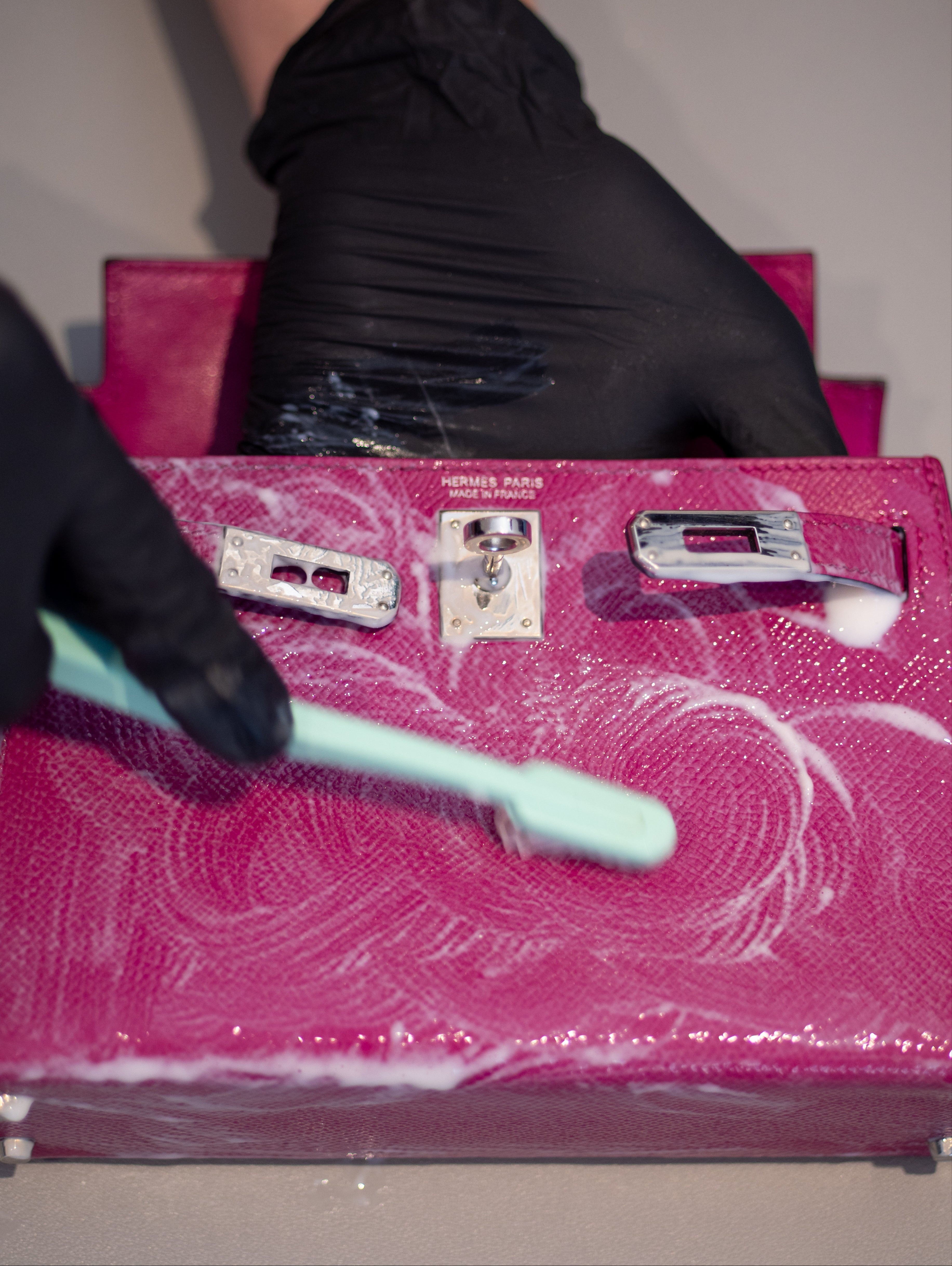 Person wearing black gloves cleaning a pink suitcase with a brush